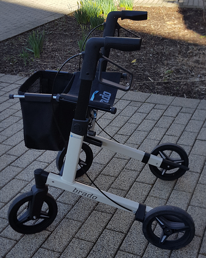 Foto: Auf dem Foto ist ein weißer Rollator abgebildet, der auf dem gepflasterten Gehweg steht.
