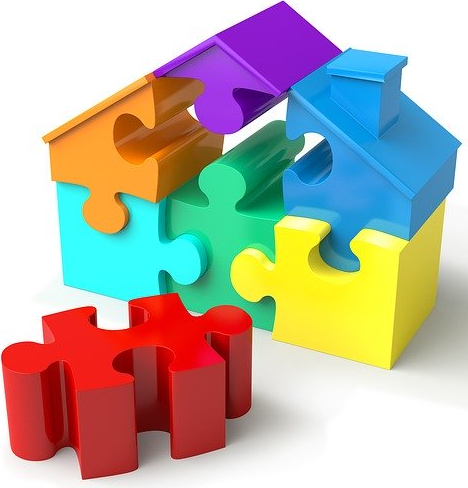 Bildbeschreibung: Das Bild zeigt ein Haus aus bunten 3 D Puzzleteilen, wobei ein rotes Teil, was im Dach des Hauses fehlt, im Bildvordergrund liegt. Ende der Bildbeschreibung.