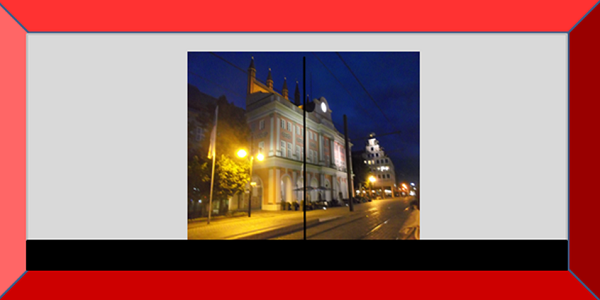 Bildbeschreibung: Das Bild 2 zeigt den Blick auf das nächtlich angeleuchtete Rostocker Rathaus durch eine Glastür ohne visuelle Kennzeichnung. Ende der Bildbeschreibung.