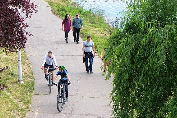 Bildbeschreibung: Bild 1 zeigt einen Fußweg, auf dem sich rechts drei Fußgänger und links vor Ihnen 2 Radfahrer befinden. Der Fußweg grenzt rechts an ein Gewässer. Ende der Beschreibung. 