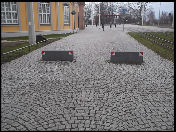Bildbeschreibung: Das Bild 12 zeigt zwei Steinquader, die mit ihrer Längsseite quer über die nutzbare Gehwegbreite angeordnet wurden. An ihren jeweils rechten und linken Seiten erhielten sie unterhalb ihrer Oberkante ein rot-weiß-schraffiertes Rechteck mit einer Kantenlänge von ca. 10 cm. Ende der Bildbeschreibung. 