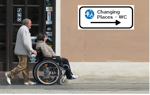 Das Bild 1 zeigt ein Mann der eine Frau im Rollstuhl schiebt vor einer hauswand mit dem Hinweis auf ein Changing Places WC.