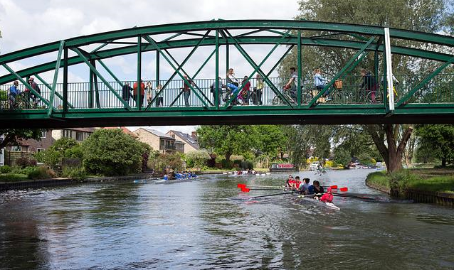 Bild 1 zeigt eine Fußgängerbrücke, auf der Menschen stehen, die über einen Fluss führt, auf dem sich Kanufahrer befinden. 