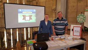 Das Bild 1 zeigt Claudia Karell und Eberhard Tölke hinter einem Tisch mit Infomaterial zur Messe im KUK Gera 2019.