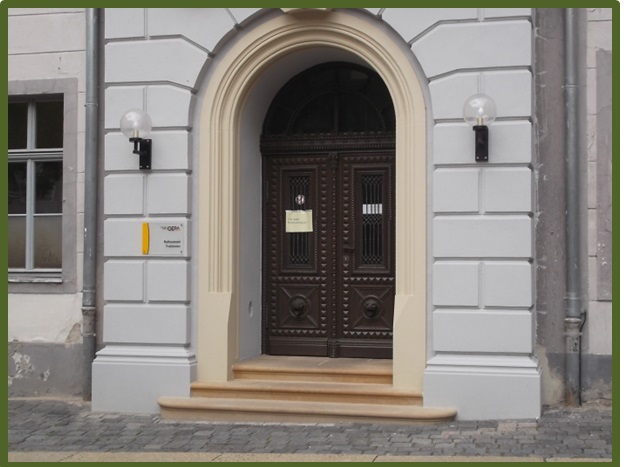 Bild 2 zeigt das Eingangsportal zu einem Gebäude mit einer Treppe ohne Handläufe sowie taktile und visuelle Orientierungshilfen.