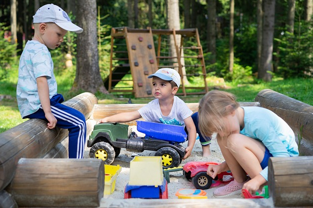 Bild 1: 3 Kinder auf Sandspielplatz, der von Baumstämmen begrenzt ist
