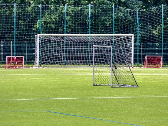 Bild 3: Fußballplatz auf Rasen mit unterschiedlich hohen und breiten Toren und Ballfang im Bildhintergrund
