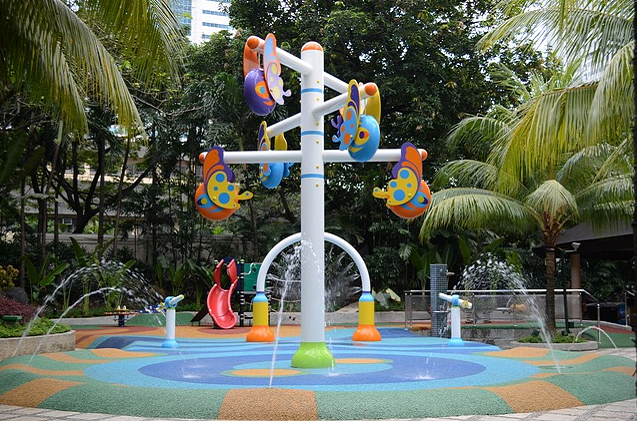 Bild 2: Wasserspielplatz (hellblauer Gummibelag), 2 Handpumpen und graue Säule in der Mitte mit bunten Figuren an den Querstreben