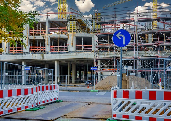 Bild 7: abgesicherte Baustelle mit Bauzäunen und Absperrschrankengittern rechts und links eines Gehweges, Baugerüst an einem Hausneubau im Bildhintergrund