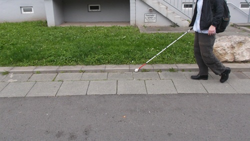 Frau mit Langstock auf einem Gehweg mit Rasenkantenstein